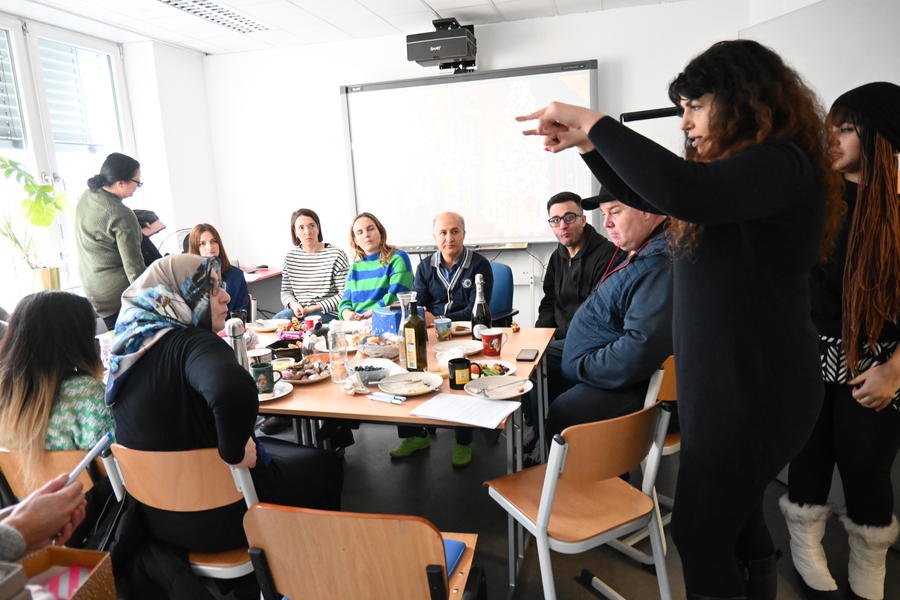 Team & Teilnehmer*innen versammeln sich in der Klasse um einen Tisch und unterhalten sich