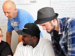         Drei Personen betrachten etwas auf eiinem Tisch unterhalb des Bildrandes  